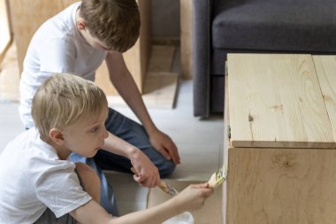 Two caucasian boys paint the table with brushes. Children help renovate the wooden cabinet. Restoring furniture