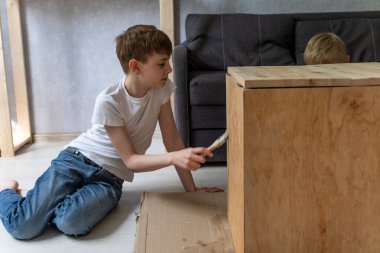 Teenage boy helps restore an old table. Child paints wooden pedestal with brush. Side view.