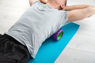 Man lies on the myofascial roller. Man performs myofascial release of hyper-movable back muscles with massage roller