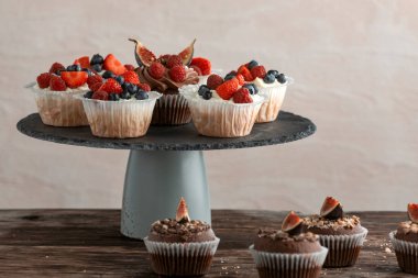 Chocolate and vanilla cupcakes with berry mix on the stand on the table. Muffin with berries. Side view.