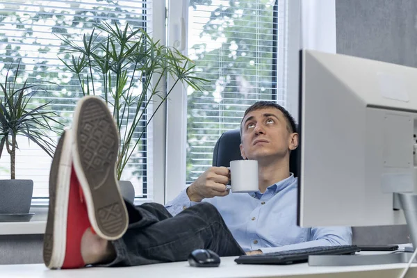 Lazy employee in office put his feet on desk and drinks coffee. Man in procrastination. Lunch time