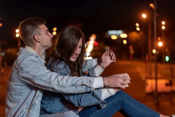 Young Couple Sitting Pavement Embracing Hugging Each Other Backdrop Lights — Stockfoto