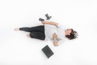 Spor kıyafetleri içinde modern bir kadın, dizüstü bilgisayar, telefon ve kamera gibi cihazlarla çevrili yatıyor. Üst görünüm