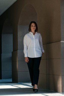 Beyaz gömlekli ve siyah pantolonlu ciddi bir kadın binanın dışında poz veriyor. Klasik kostümlü kadın portresi.