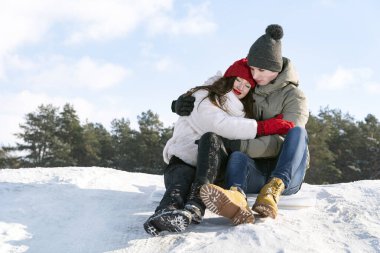 Genç mutlu aşıklar oturur ve sarılır. Kış ormanı ve mavi gökyüzünün arka planında. Kış güneşli gün.