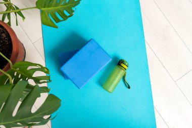 Yoga minderinin üstünde mor yoga tuğlaları ve su şişesi var. Jimnastik ve esneme aletleri