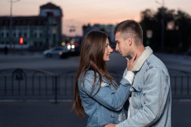 Genç, beyaz, güzel bir çift şehrin arka planında sarılıyor. Yan görünüm.