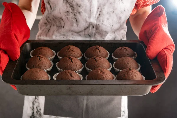 Hands of cook with just baked chocolate hot cupcakes. Homemade muffins on baking sheet