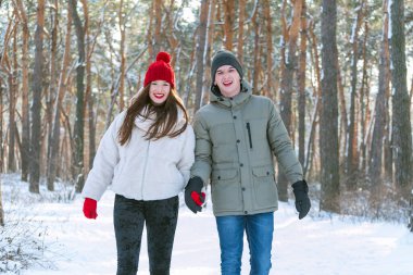 Genç çift kışın ormanda yürür ve el ele tutuşur. Mutlu gülümseyen aşıklar karlı parkta yürürler.