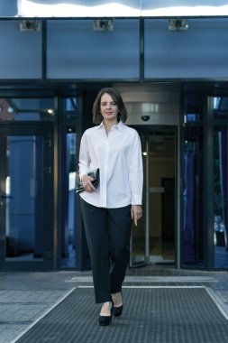 Modern ofis merkezinin arka planına karşı resmi iş kıyafetleri içinde başarılı genç bir kadın. Beyaz gömlekli bir iş kadını.