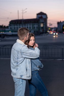 Genç ve güzel bir çift, gece şehir geçmişinde birbirlerine sarılıyorlar. Dikey çerçeve.