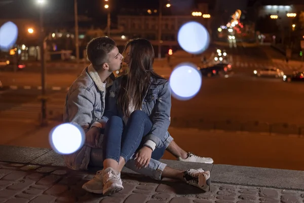 Birbirlerine aşık genç bir çift, akşam vakti sarılıp öpüşüyorlar. Bokeh