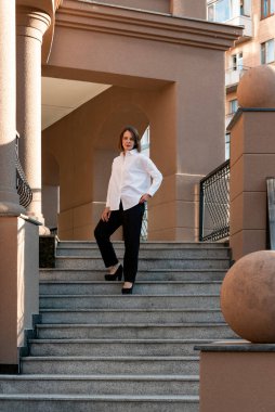 Mimari binanın merdivenlerinde çalışan bir iş kadını. Kadın klasik tarz, gömlek ve pantolon giyiyor.