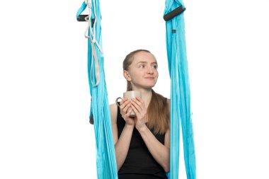 Spor hamağında oturmuş yoga derslerinin başlamasını bekleyen bir fincan çayla güzel bir kızın portresi. Beyaz arkaplan.