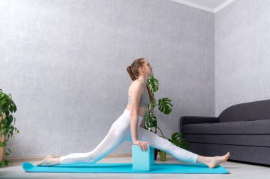 Beyaz eşofmanlı genç kadın tuğlalarla yoga egzersizleri yapıyor. İp egzersizleri. Pratik esnekliği