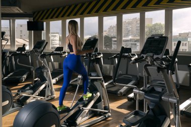 Spor salonundaki kız yörüngede egzersiz yapıyor. Eliptik simülatörde spor. Büyük boş spor salonu.