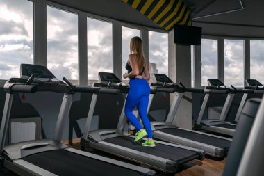 Spor sarışın kız boş modern spor salonundaki koşu bandında koşuyor. Çalışan pistte kardiyo çalışması.
