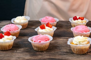 Kremalı ve çilekli kekler. Tahta masada ev yapımı vanilyalı kekler.
