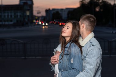 Adam akşam vakti sevgilisine sarılıyor. Güzel genç bir çift gece sokakta dikiliyor.