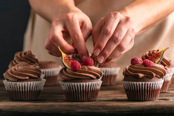 Pastry chef decorates cupcakes with raspberries and figs. Close up photo of muffin preparation