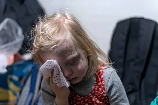 KHARKOV, UKRAINE - 3 Mart 2022: küçük bitkin kız bomba sığınağında oturan mendille yüzünü siliyor. Çocuklar bodrumlarda saklanır.