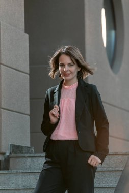 Ceketli başarılı genç kadın merdivenlerden aşağı iniyor. Siyah takım elbiseli, kısa saçlı kız.