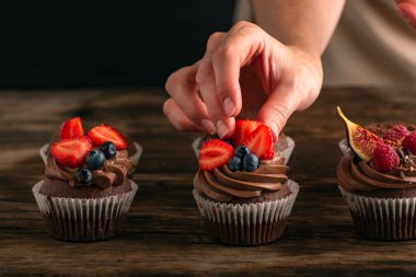 Kadınların elleri çikolatalı kekleri taze çilekle süslüyor. Meyveli kek pişirme işlemi