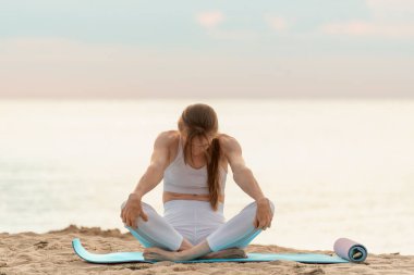 Genç bir kadın sabahları deniz arka planında egzersiz yapıyor. Nefes alıştırması. Kız plajda yoga yapıyor.