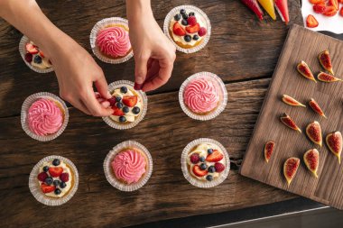 Pembe kremalı kekler ve taze mevsimlik meyveli kekler ahşap masada. Eller çöreği alsın.