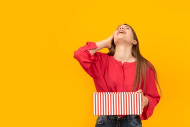 Genç kız elinde açık bir hediye kutusu tutuyor ve kafası geriye doğru savrulup gülüyor. Sarı arkaplanda portre