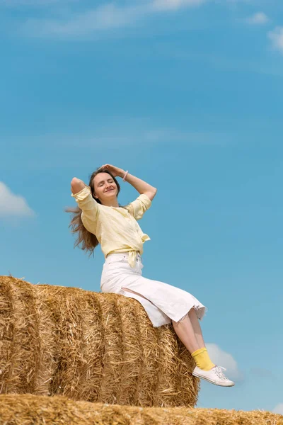 Sarı gömlekli ve samanlıkta parlak çoraplı mutlu genç bir kadının dikey portresi.