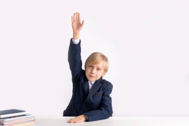 Birinci sınıftaki üniformalı çocuk öğretmenlerin sorularına cevap vermek için elini kaldırdı. Her şeyi bilen çocuğun portresi. Beyaz arkaplanda izole