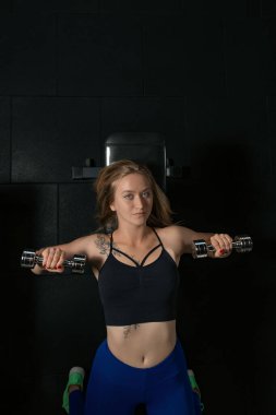 Genç atletik kadın sırtüstü uzanıyor ve spor salonunda antrenman yapıyor doğrudan kameraya bakıyor. Üst Manzara. Göğüs kaslarınızı güçlendirmek için dambıllarla egzersiz yapın.