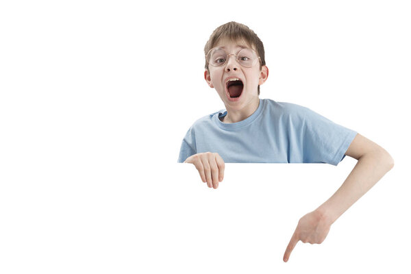 Screaming teenage boy points his finger down at empty space. Portrait of impressed schoolboy isolated on white background. Copy space