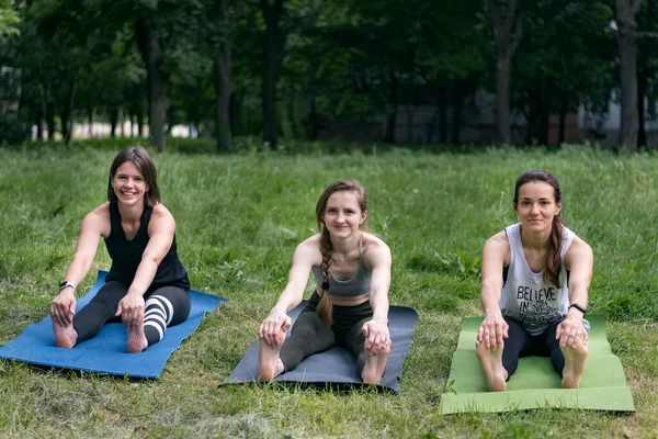 Parkta grup çalışması sırasında esneme egzersizi yapan gülümseyen genç kadınlar. Fitness ve sağlıklı yaşam tarzı