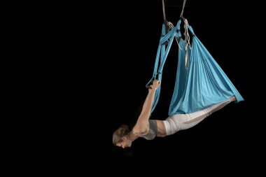 Sporcu kadının tam boy görüntüsü baş aşağı asılı dururken aero uçuş yoga pozisyonu uyguluyor. Siyah arkaplan.