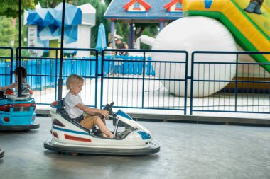 Küçük çocuk lunaparkta çarpışan araba kullanıyor. Genç sürücüler go kart yarışında çocuk parkında eğleniyorlar.