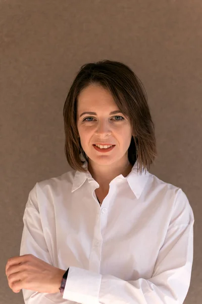 Young woman with Bob haircut in white shirt on beige background. Successful businesswoman