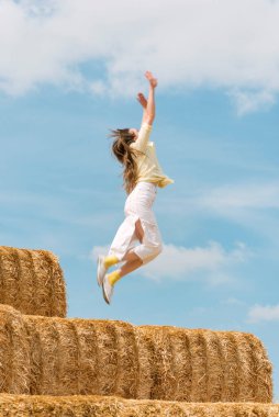 Mutlu genç kadın samanlıktan atlıyor. Kaygısız kız mavi gökyüzü arka planında çiftlikte eğleniyor.