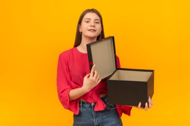 Genç bayanın elinde açık bir hediye var. Parlak sarı arka planda büyük siyah kutulu bir kadın. Şaşırmış hevesli kız..