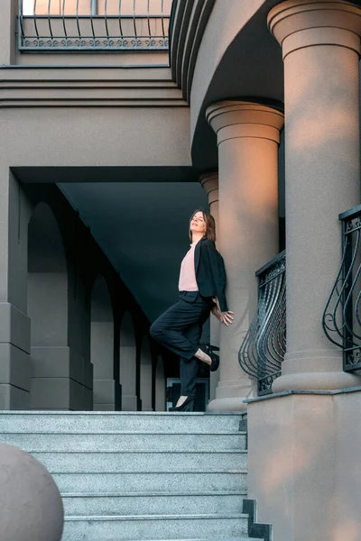 Takım elbiseli ve topuklu ayakkabılı bir kadın duvara yaslanmış. Tam boy portre. Modern başarılı kadın.