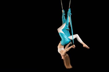 Beyaz spor giyimli kadın hamaklı havadan ters çevirme anti-yerçekimi yogası uyguluyor. Yan görünüm. Siyah arkaplanda izole edilmiş..