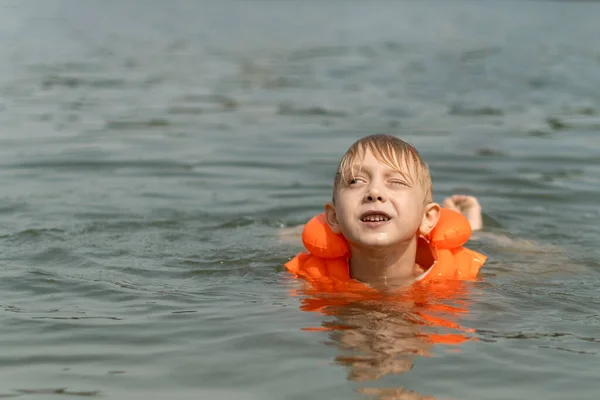 Little boy swims in lake or the sea in an inflatable vest. Child in life jacket in the water