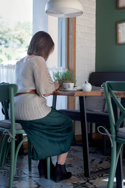 Woman with a smartphone and sits at table in cafe with cup of coffee or tea. Business woman during lunch. Vertical frame