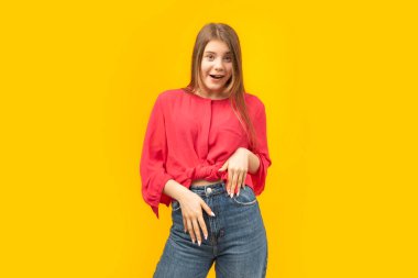 Sarı arka planda kırmızı bluz ve kot pantolonlu genç kız. Şaşırmış genç esmer kadın portresi