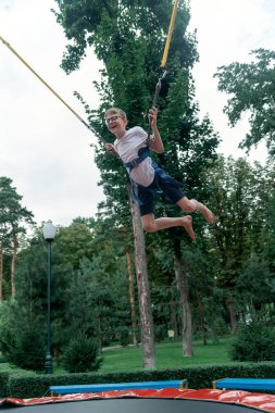 Trambolinde bungee jumping yapan mutlu çocuk. Bir eğlence parkındaki genç eğleniyor. Hafta sonu eğlence parkında. Dikey çerçeve