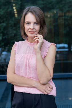 Dışarıdaki pembe bluzlu orta yaşlı kadının portresi. Kısa saçlı esmer iş kızı..