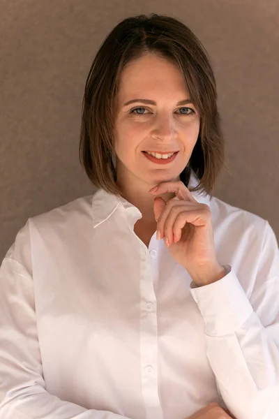 Young woman with Bob haircut in formal white shirt on beige background. Successful businesswoman