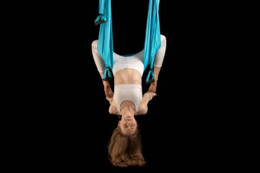 Beyaz spor giysili genç kız yoga yapıyor ve siyah arka planda izole edilmiş esneme hareketleri yapıyor. Hava anti-yerçekimi yogası için hamak kullanan bir kadın.