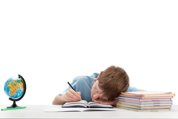 带着眼镜的男中学生做作业时很累 男孩睡在他的书桌前 描绘出一个有着白色背景的疲倦男孩的形象 — 图库照片